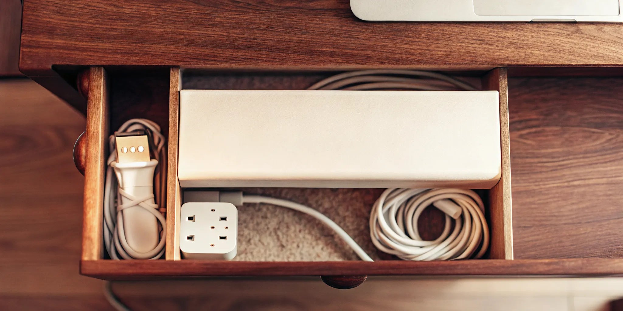 A cord organizer box neatly storing a power strip and cables inside a wooden desk drawer.