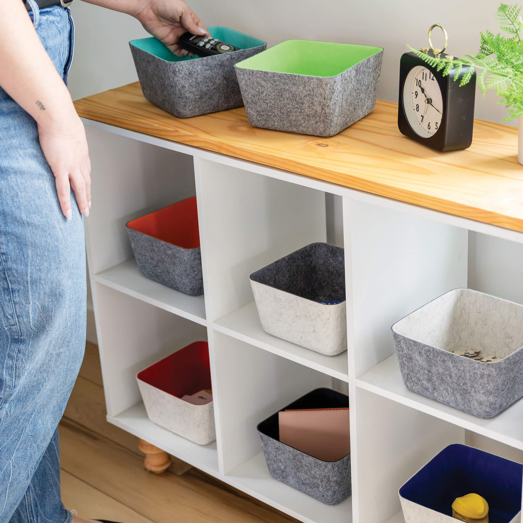 Colorful recycled felt organizing sorting storage bins on a wooden shelf with a person partially visible.