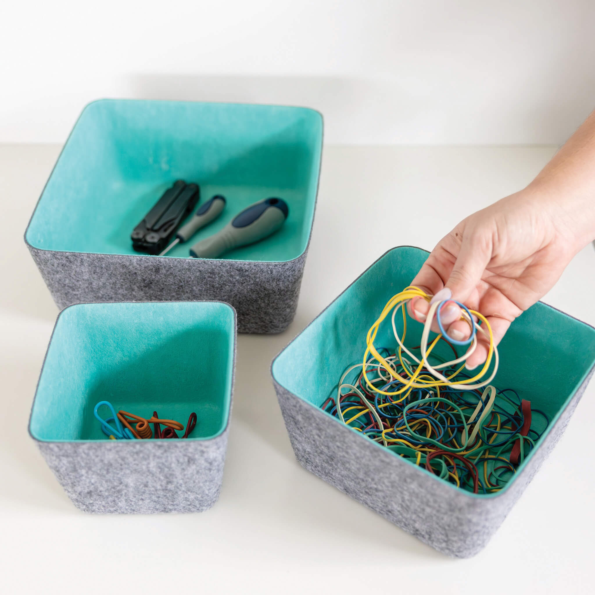 Three square recycled felt organizing sorting storage bins with blue interior and gray exterior, with organized items.