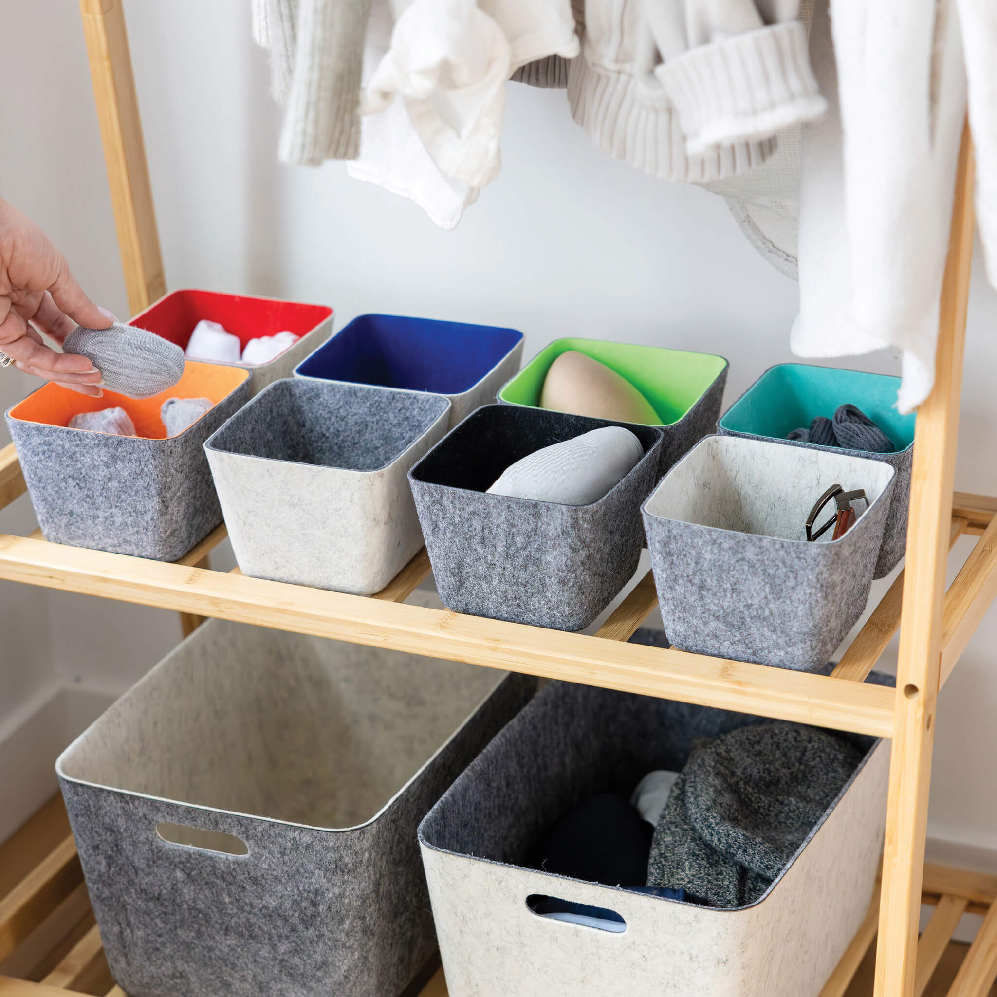 Recycled felt organizing sorting storage bins  in various colors on a wooden shelf with clothes in the background.