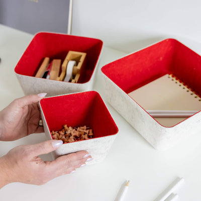Red and white recycled felt organizing sorting storage bin with red interior and cream exterior with items inside on a white surface.